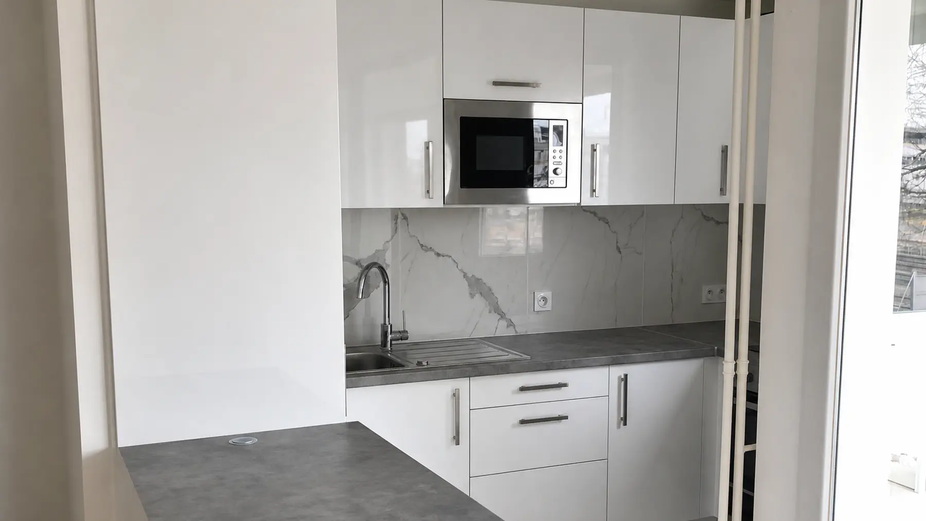 Cuisine blanche livrée par Izem Rénovation, crédence effet marbre, plan de travail gris anthracite, colonne micro-ondes encastrée et bar en retour sur le séjour