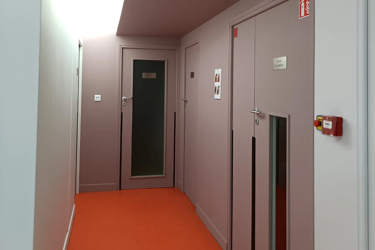 Couloir de bureaux après rénovation : murs et plafond peints en vieux rose, sol souple orange, portes coupe-feu et déclencheur manuel d'alarme incendie le long du dégagement