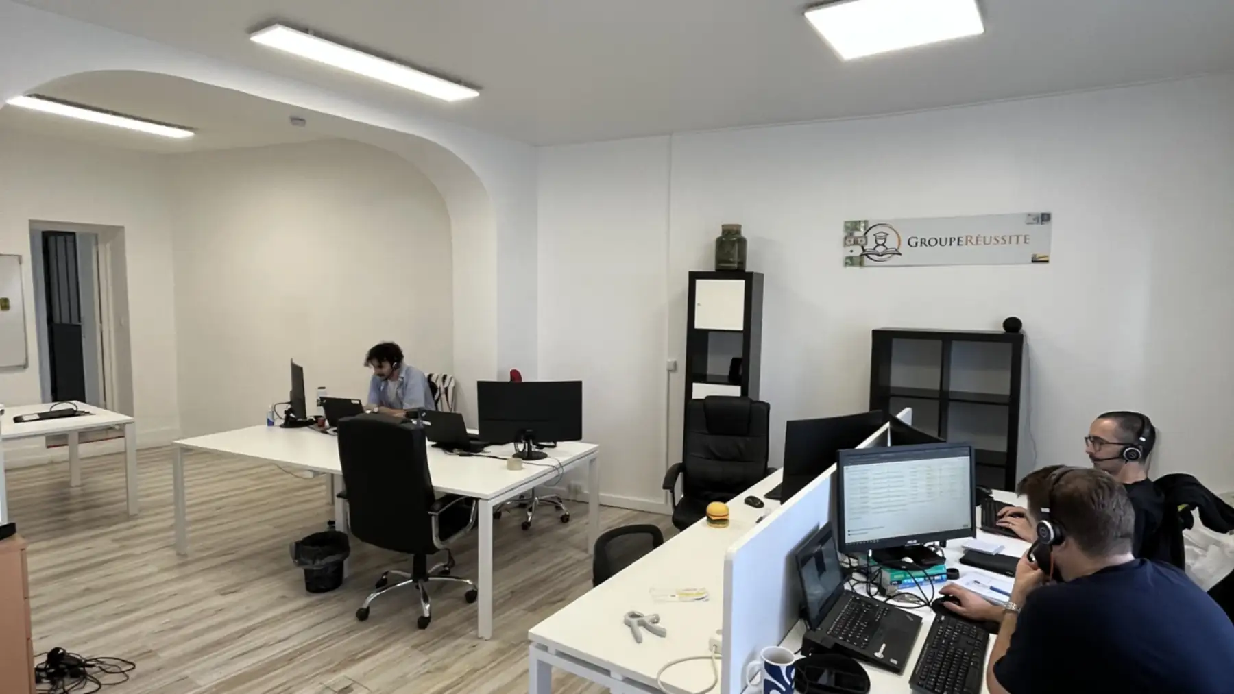 Plateau de bureaux livré après rénovation : murs blancs, sol stratifié clair, dalles lumineuses encastrées au plafond et niche cintrée conservée au fond de la pièce