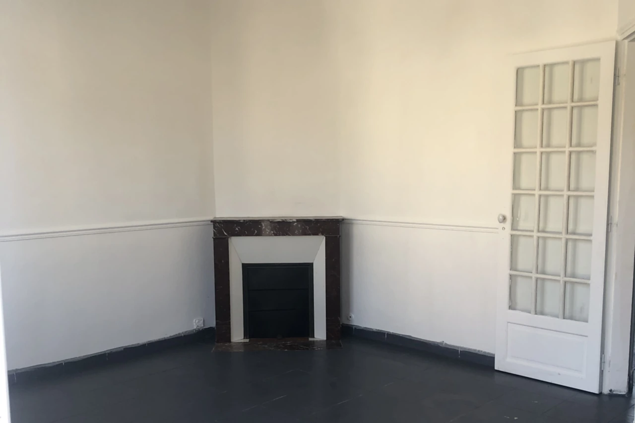 Séjour de maison livré après rénovation : murs repeints en blanc avec cimaise, cheminée de marbre veiné conservée, parquet peint en gris anthracite et porte vitrée à petits carreaux d'origine